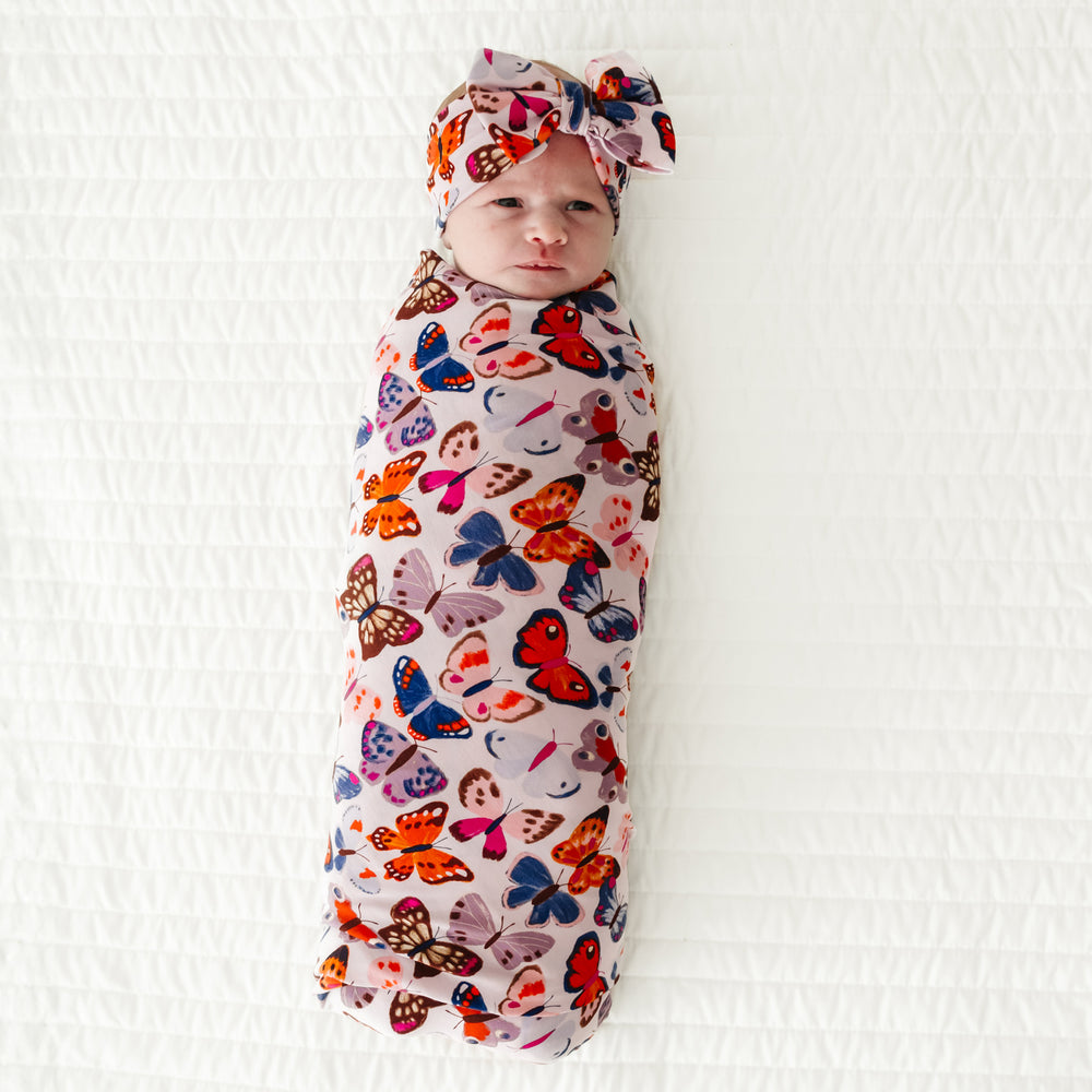 Infant swaddled in a Butterfly Kisses swaddle & luxe bow headband set