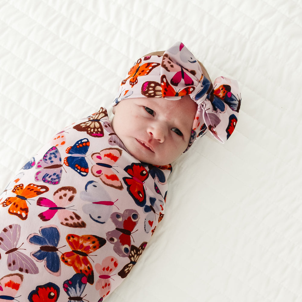 Close up image of an infant swaddled in a Butterfly Kisses swaddle & luxe bow headband set