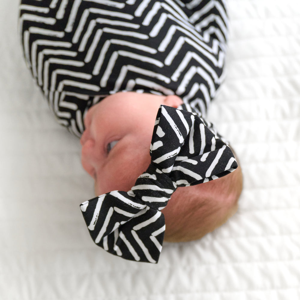 Close up image of a child swaddled in a Monochrome Chevron swaddle and luxe bow headband set
