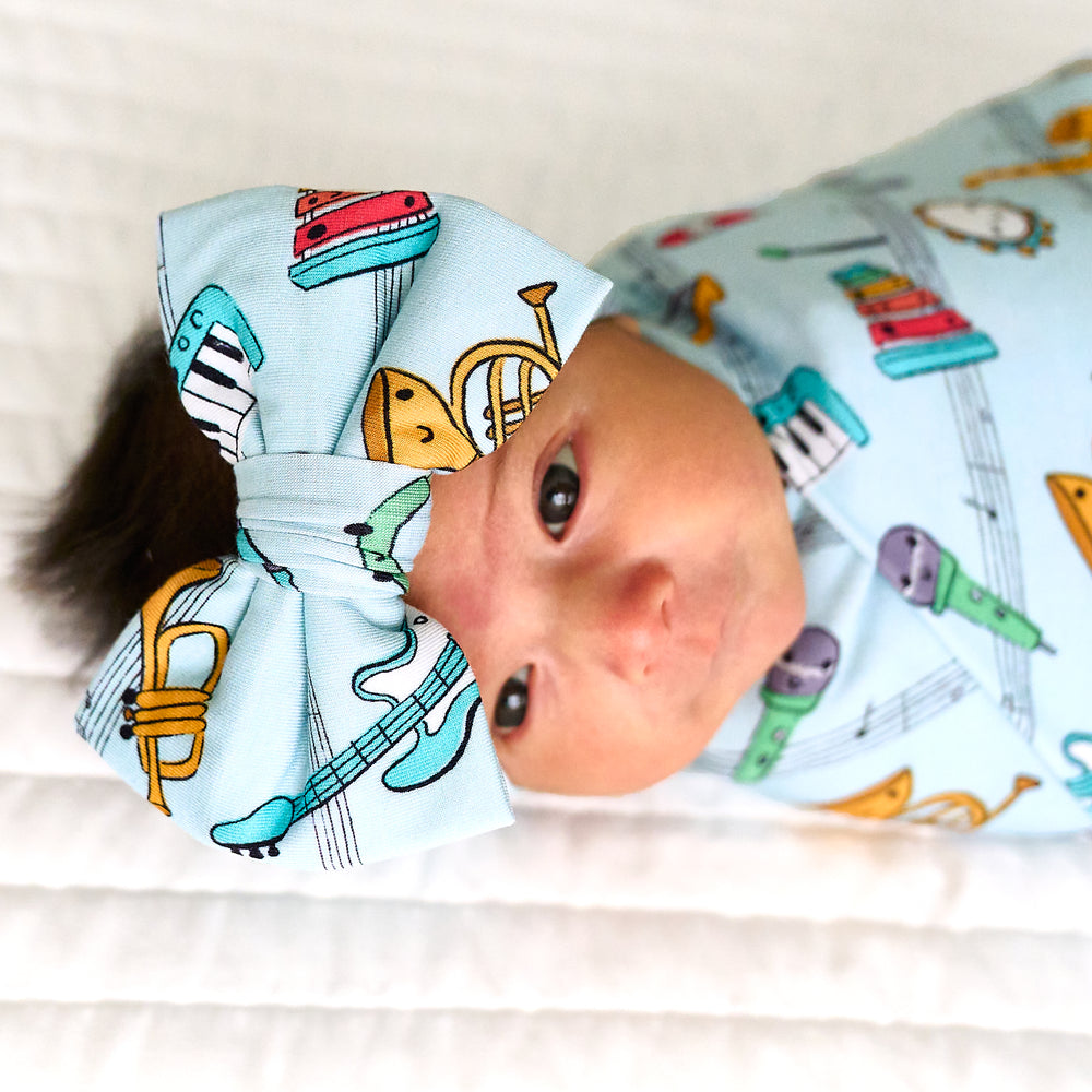Close up image of a child swaddled in a Play Along swaddle and luxe bow headband set