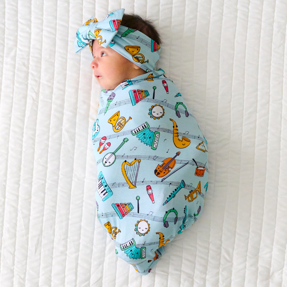 Child swaddled in a Play Along swaddle and luxe bow headband set