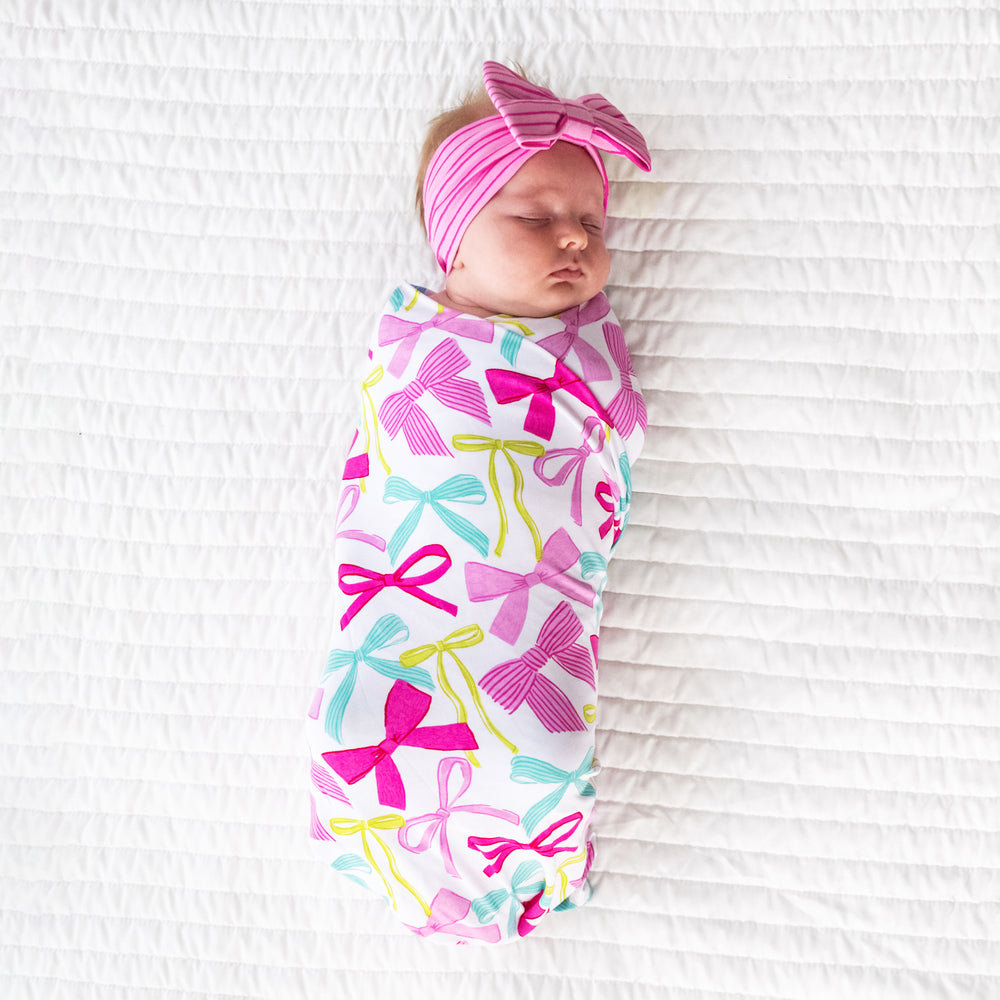 Child swaddled on a bed in a Ribbons and Bows swaddle and luxe bow headband set