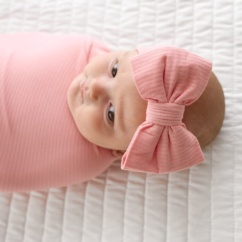 Close up image of baby wearing the Bubblegum Ribbed Swaddle & Luxe Bow Headband Set