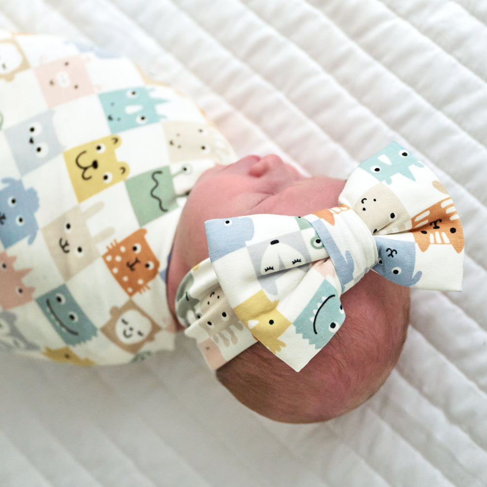 Close up image of an infant swaddled in a Check Mates swaddle and luxe bow headband set