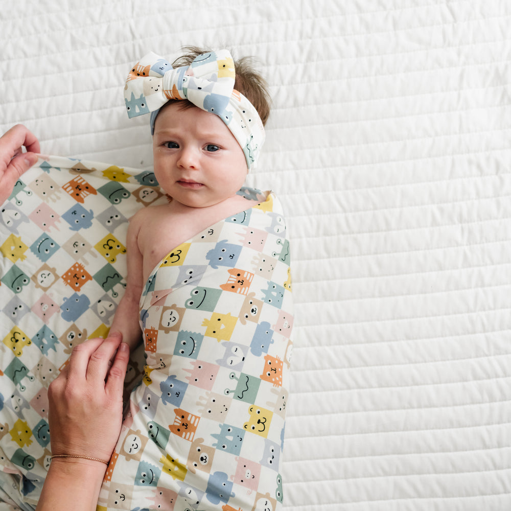 Child being swaddled in a Check Mates swaddle and luxe bow headband set