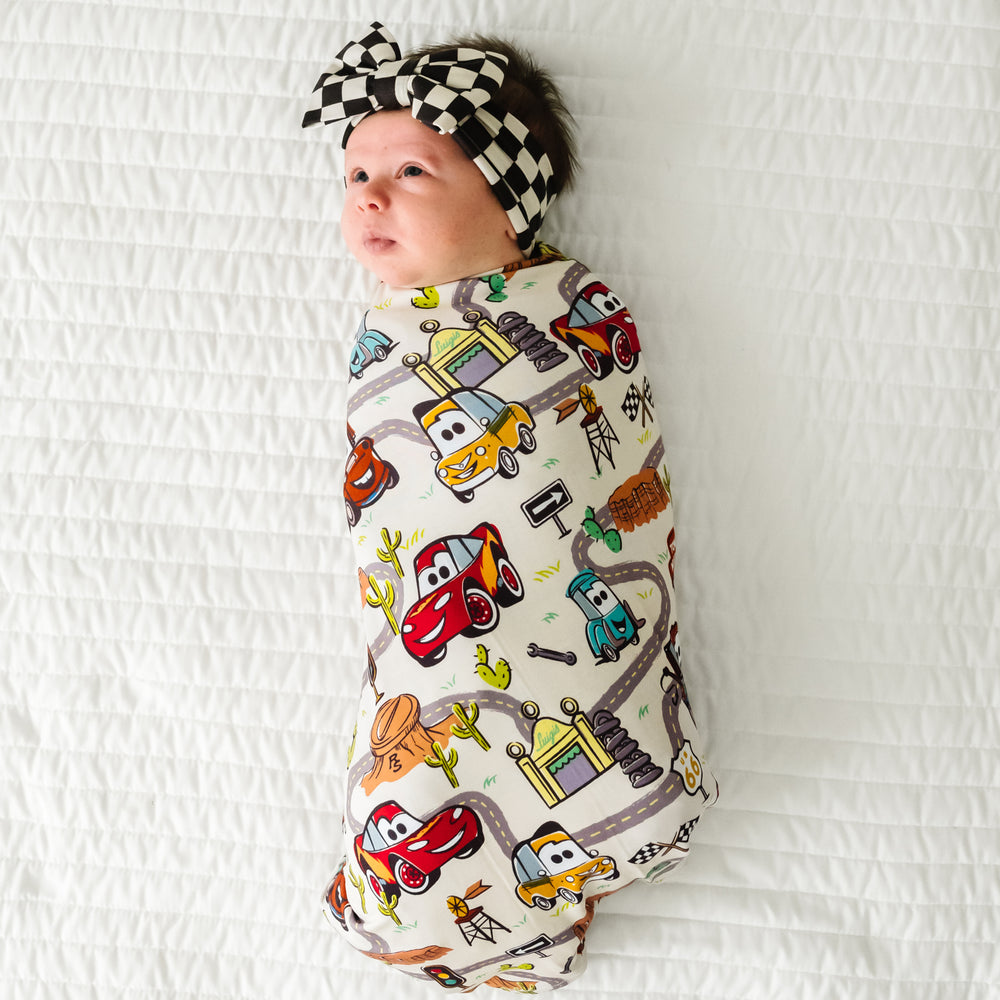 Alternate image of a child laying on a bed swaddled in a Radiator Springs swaddle and luxe bow set