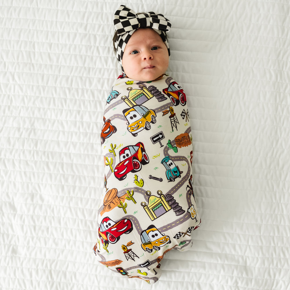 Child laying on a bed swaddled in a Radiator Springs swaddle and luxe bow set
