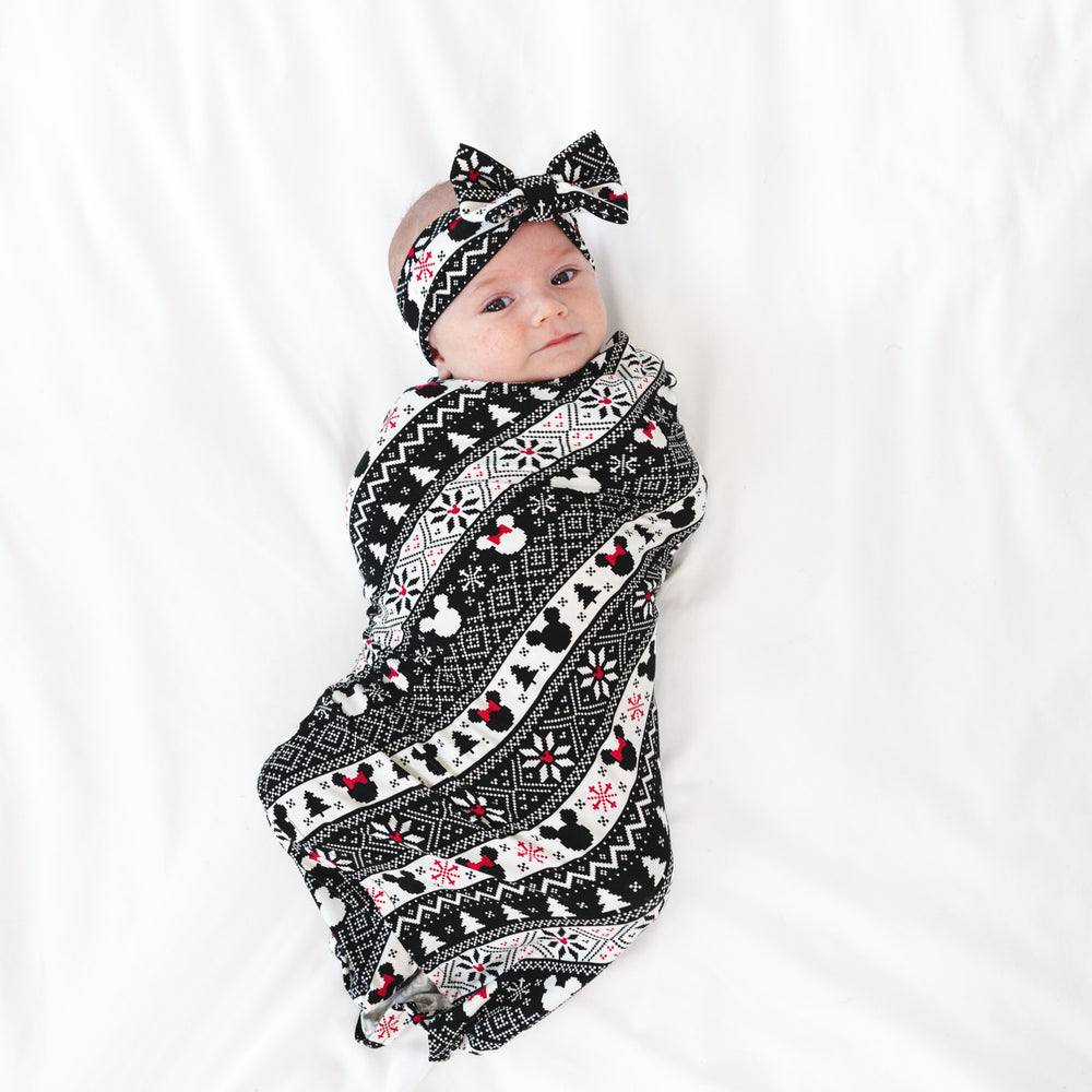 Child laying on a bed wearing a Mickey Fair Isle swaddle and luxe bow headband set