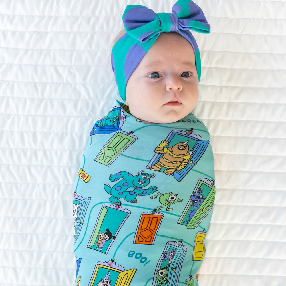 Close up top view image of baby laying down while in the Disney Monsters, Inc. Scream Team Swaddle & Luxe Bow Headband Set