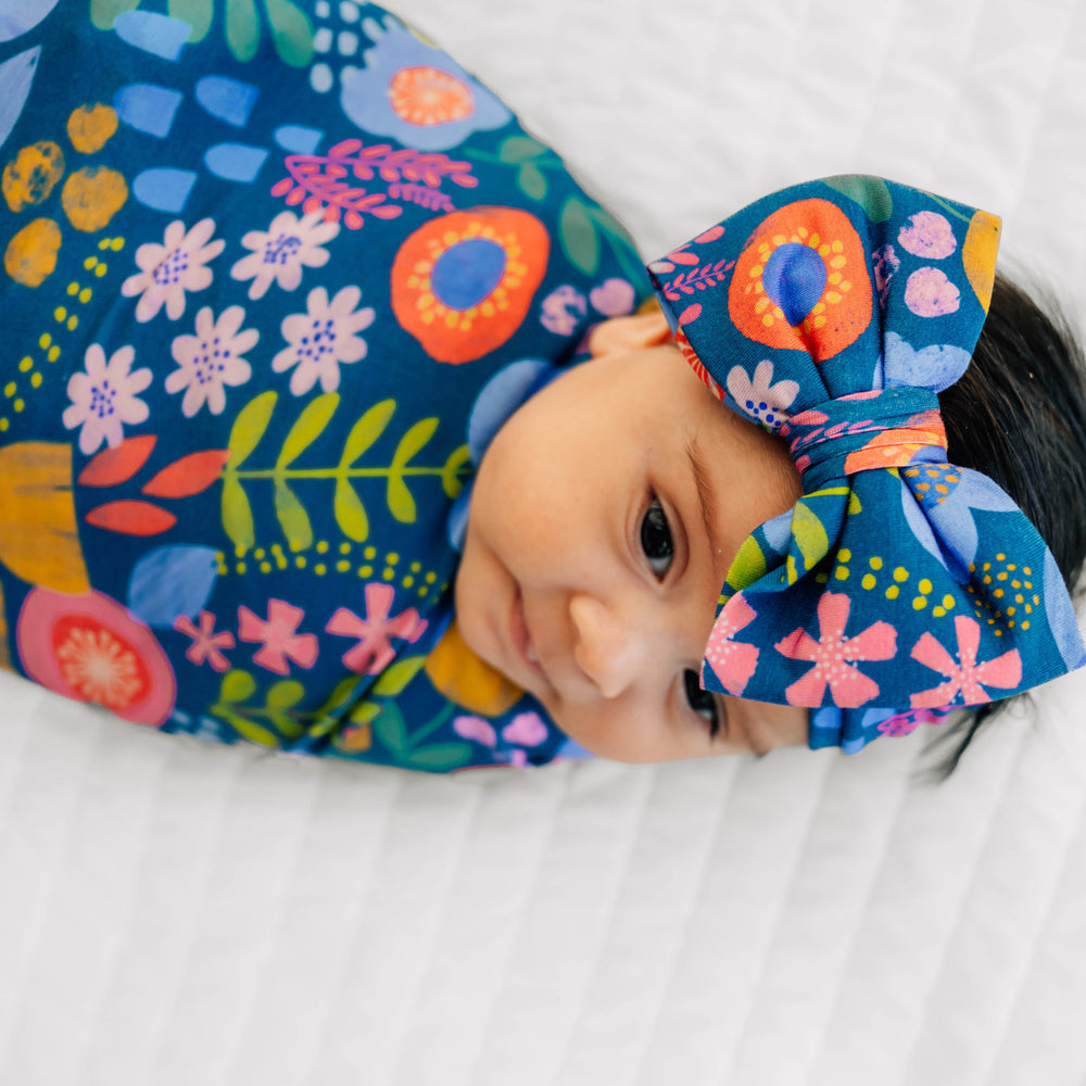 Alternative close up image of baby laying while wearing the Folk Floral Swaddle & Luxe Bow Headband Set