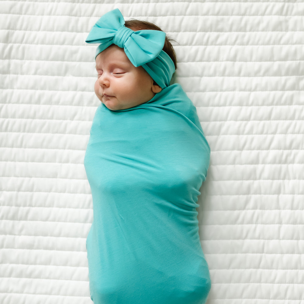 Image of a child swaddled in a Glacier Turquoise swaddle and luxe bow set 