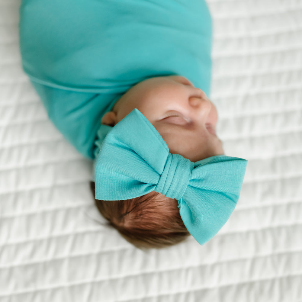 Close up image of a child swaddled in a Glacier Turquoise swaddle and luxe bow set