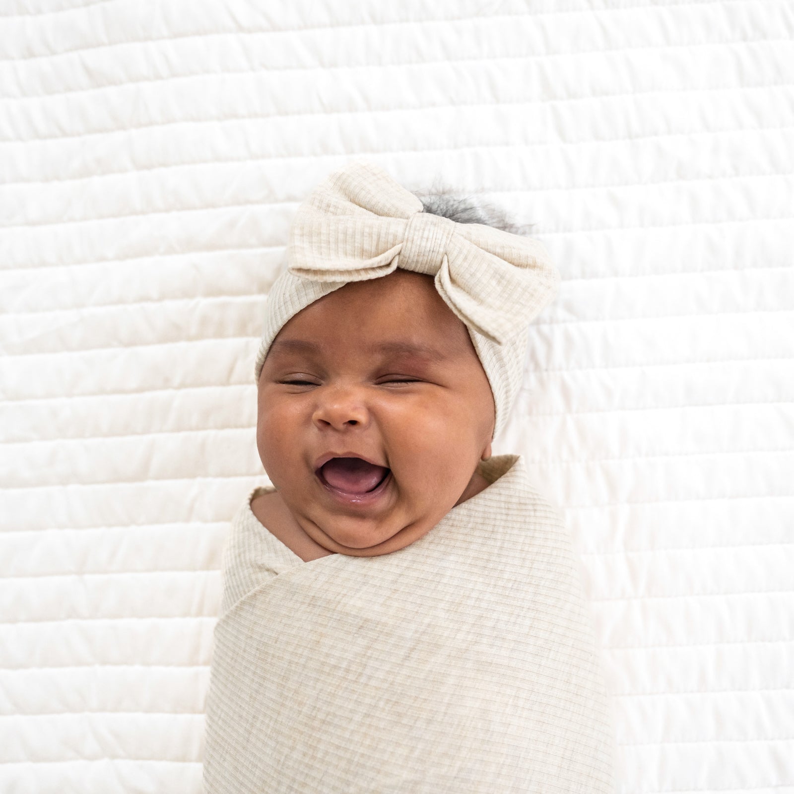 Close up immage of a child swaddled in a Heather Oatmeal Ribbed Swaddle and Luxe Bow Headband Set