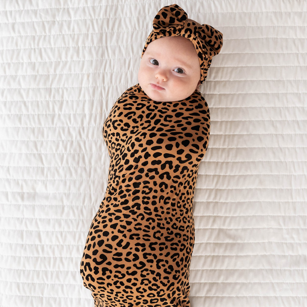 Top view image of baby laying down in the Classic Leopard Swaddle & Luxe Bow Headband Set