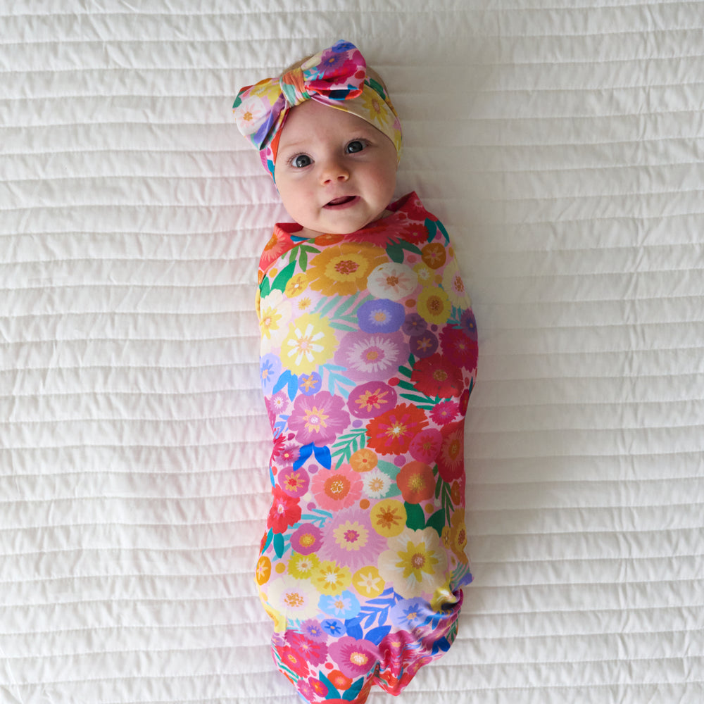 Infant swaddled in a Rainbow Blooms swaddle and luxe bow headband set