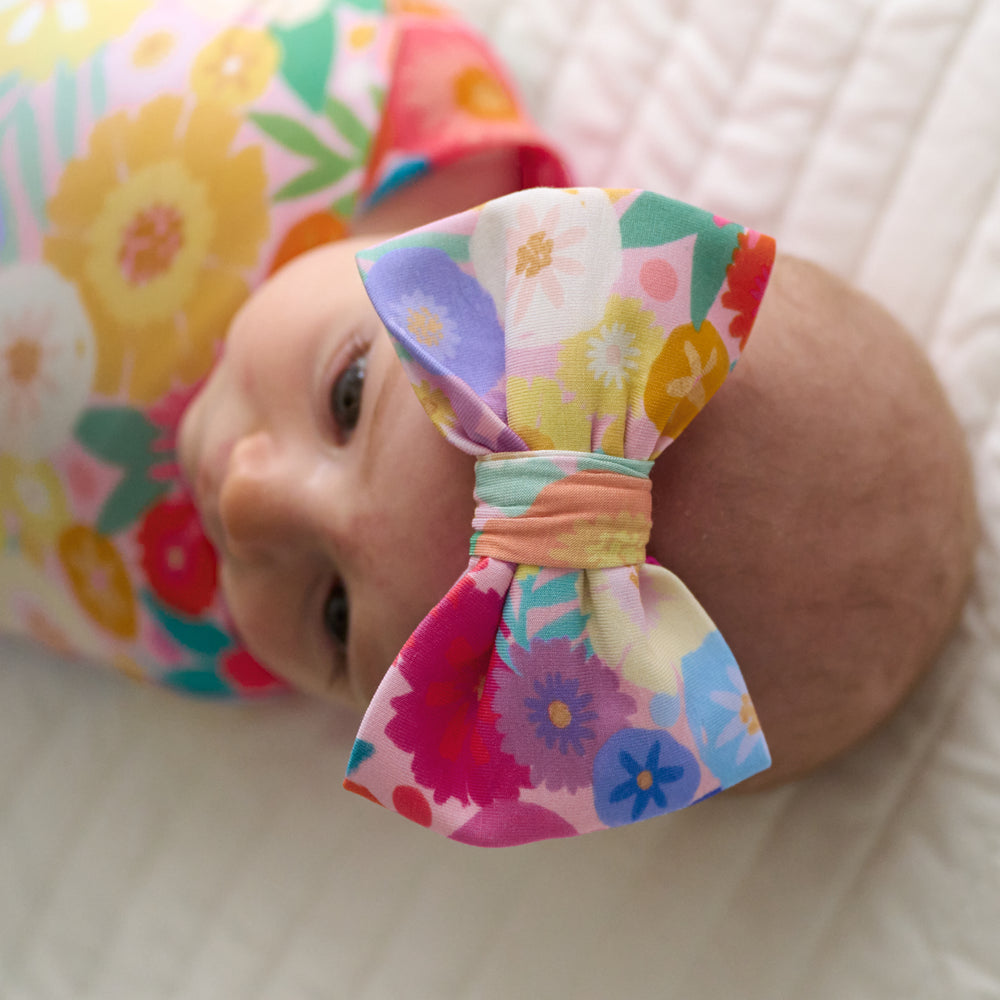 Close up image of an infant swaddled in a Rainbow Blooms swaddle and luxe bow headband set