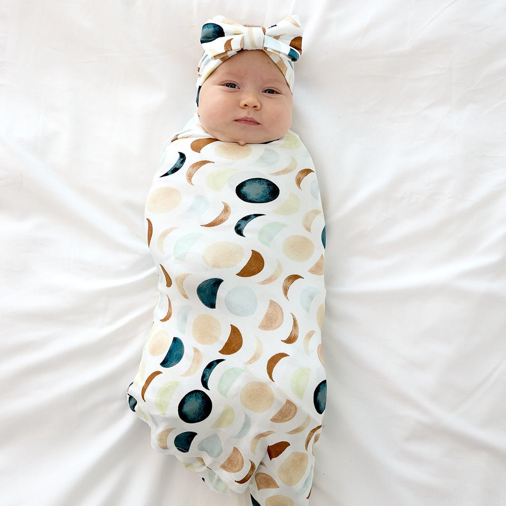 baby smiling wearing luna neutral swaddle with luxe bow headband laying down