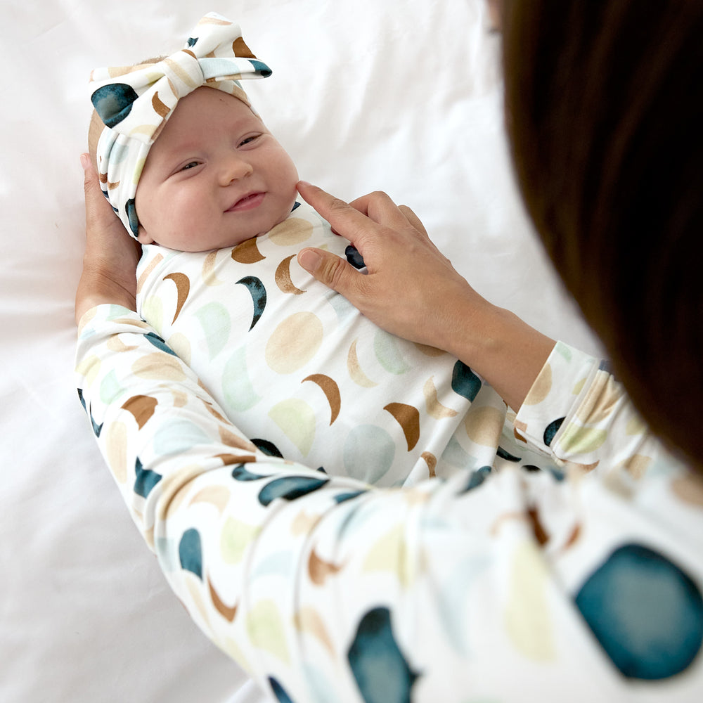 baby smiling wearing luna neutral swaddle with luxe bow headband with mom gently touching her cheek