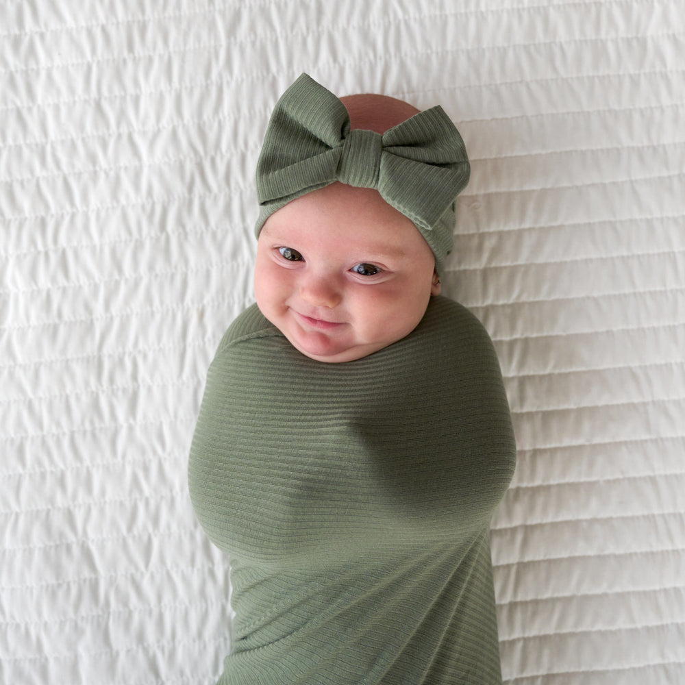 Close up image of baby smiling in the bow headband within the Moss Ribbed Swaddle & Luxe Bow Headband Set