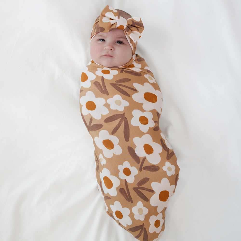 Image of a child swaddled in a Daisy Daydream swaddle and luxe bow headband set