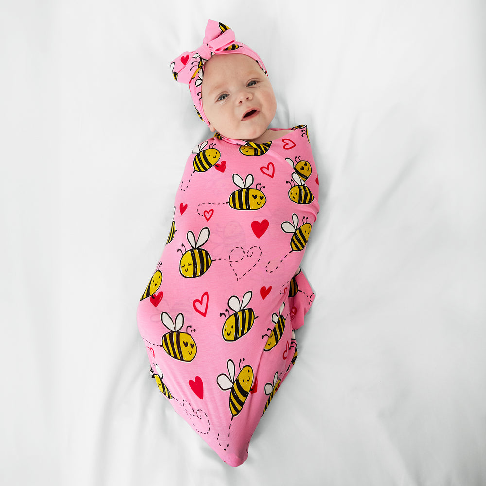 Image of a child swaddled in a pink Bee Mine swaddle set on a bed