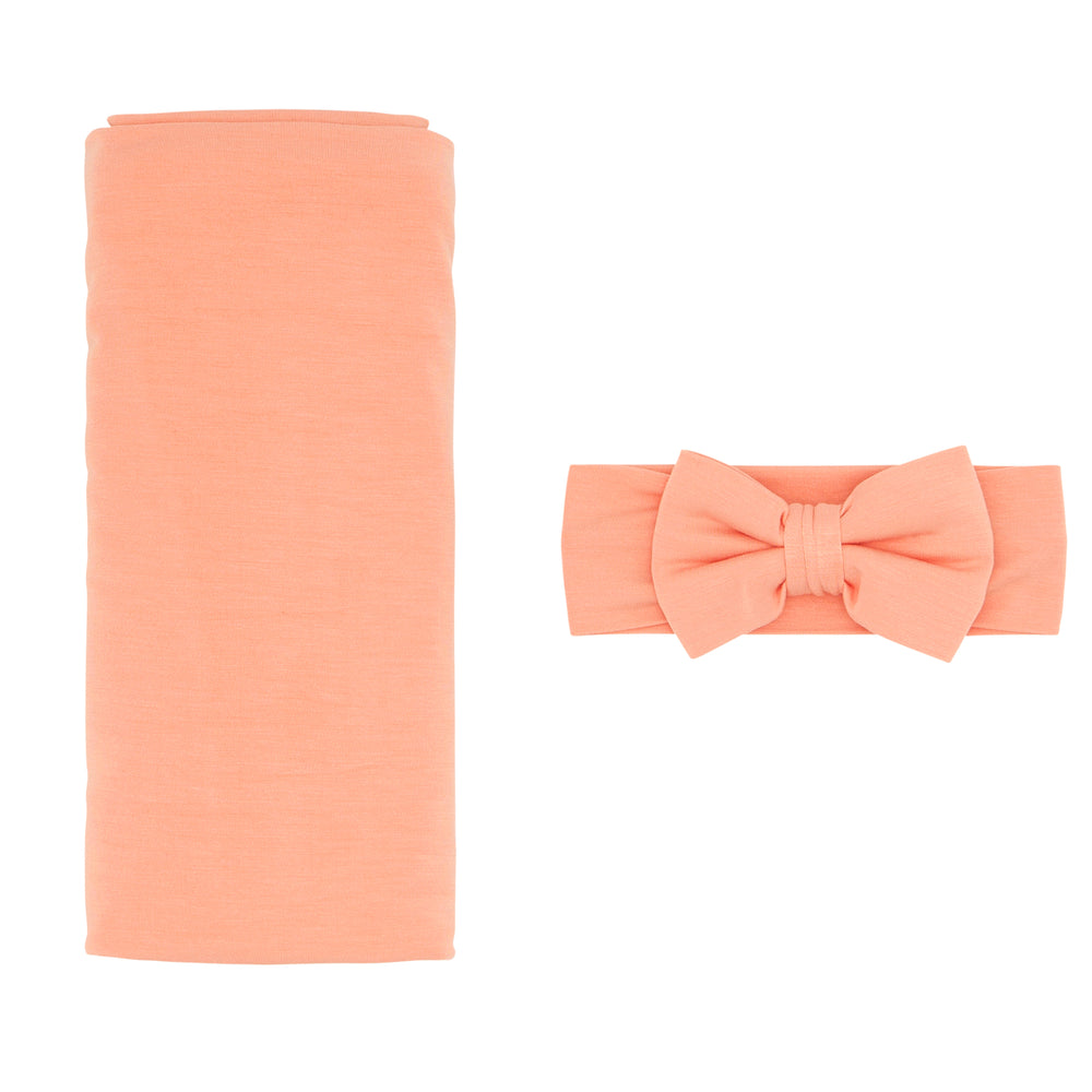 Flat lay image of a Peach swaddle and luxe bow headband set