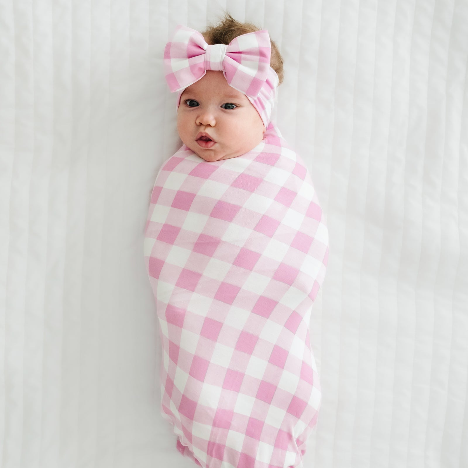 Child swaddled in a Pink Gingham swaddle and luxe bow headband set