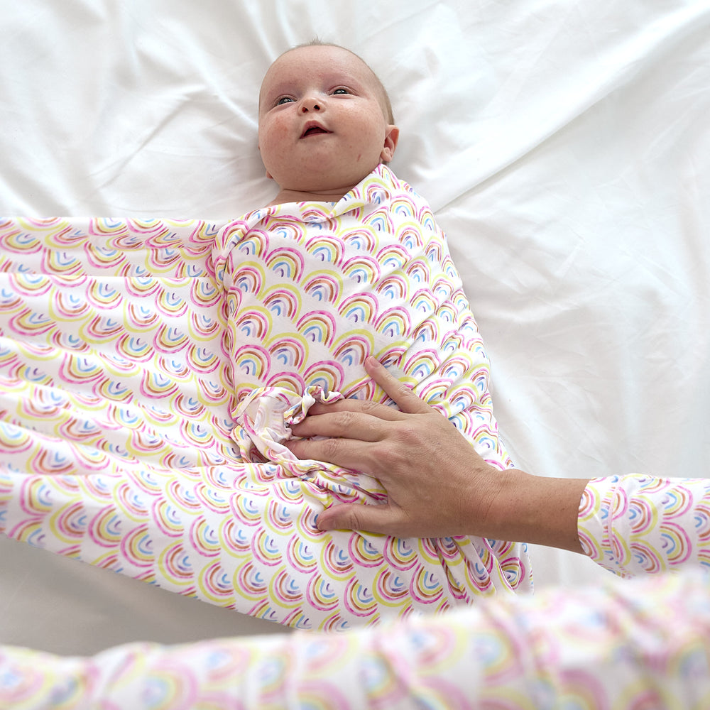 baby laying on bed getting swaddled into the  pastel rainbows swaddle set with headband