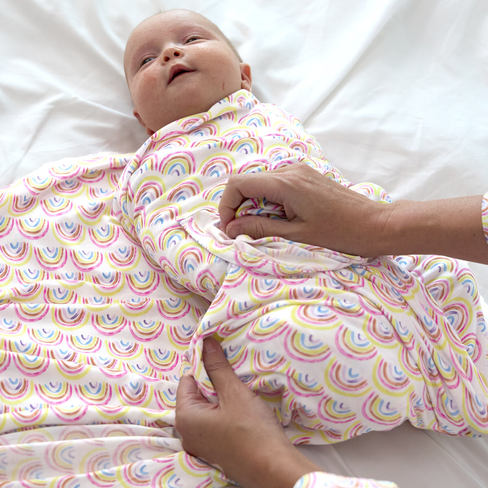 baby laying on bed getting swaddled and tucked into the  pastel rainbows swaddle set with headband 