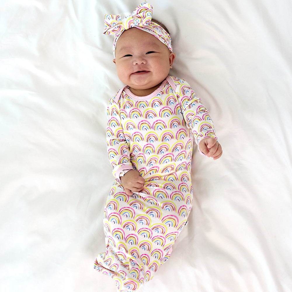 baby smiling wearing the pastel rainbows gown and a luxe bow