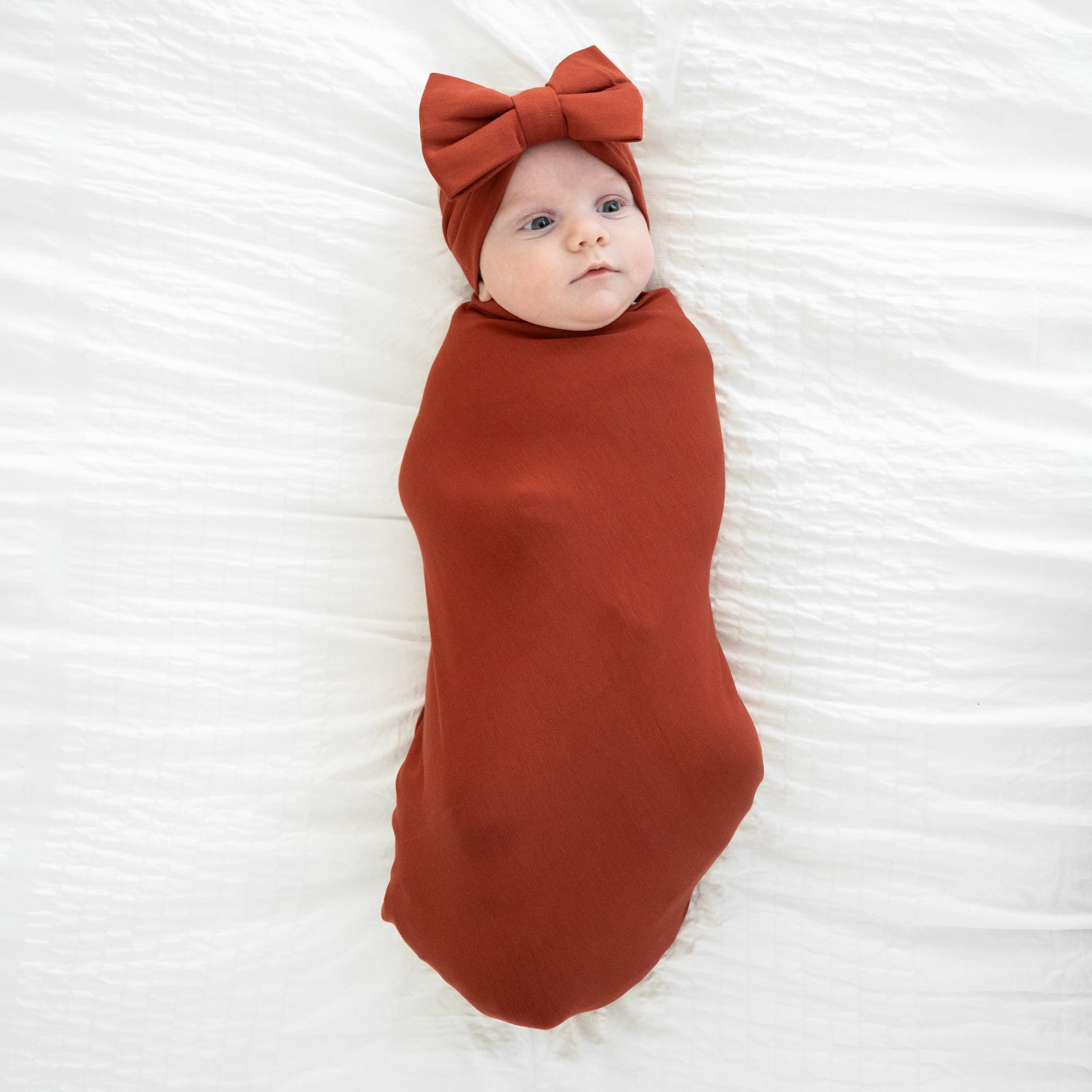 image of a child swaddled in a Cozy Rust swaddle and luxe bow headband set