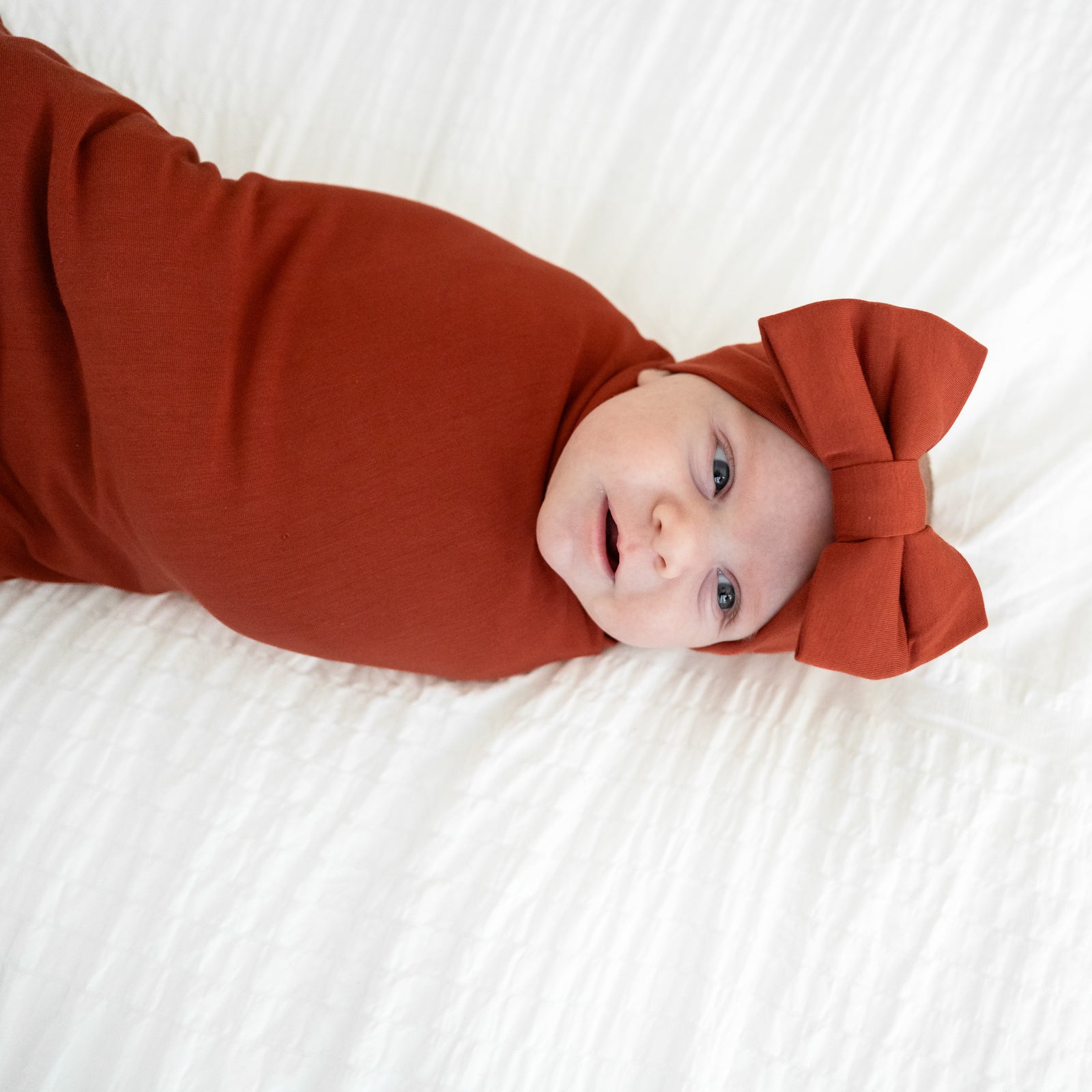 Close up image of a child swaddled in a Cozy Rust swaddle and luxe bow headband set