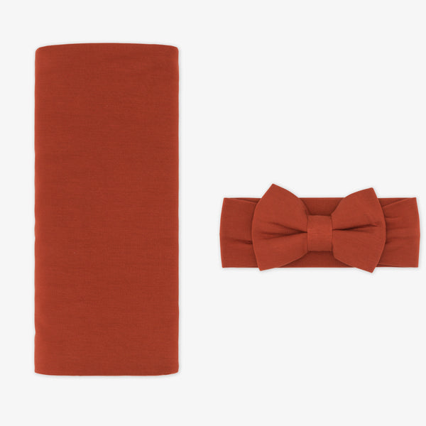 Flat lay image of a Cozy Rust swaddle and luxe bow headband set