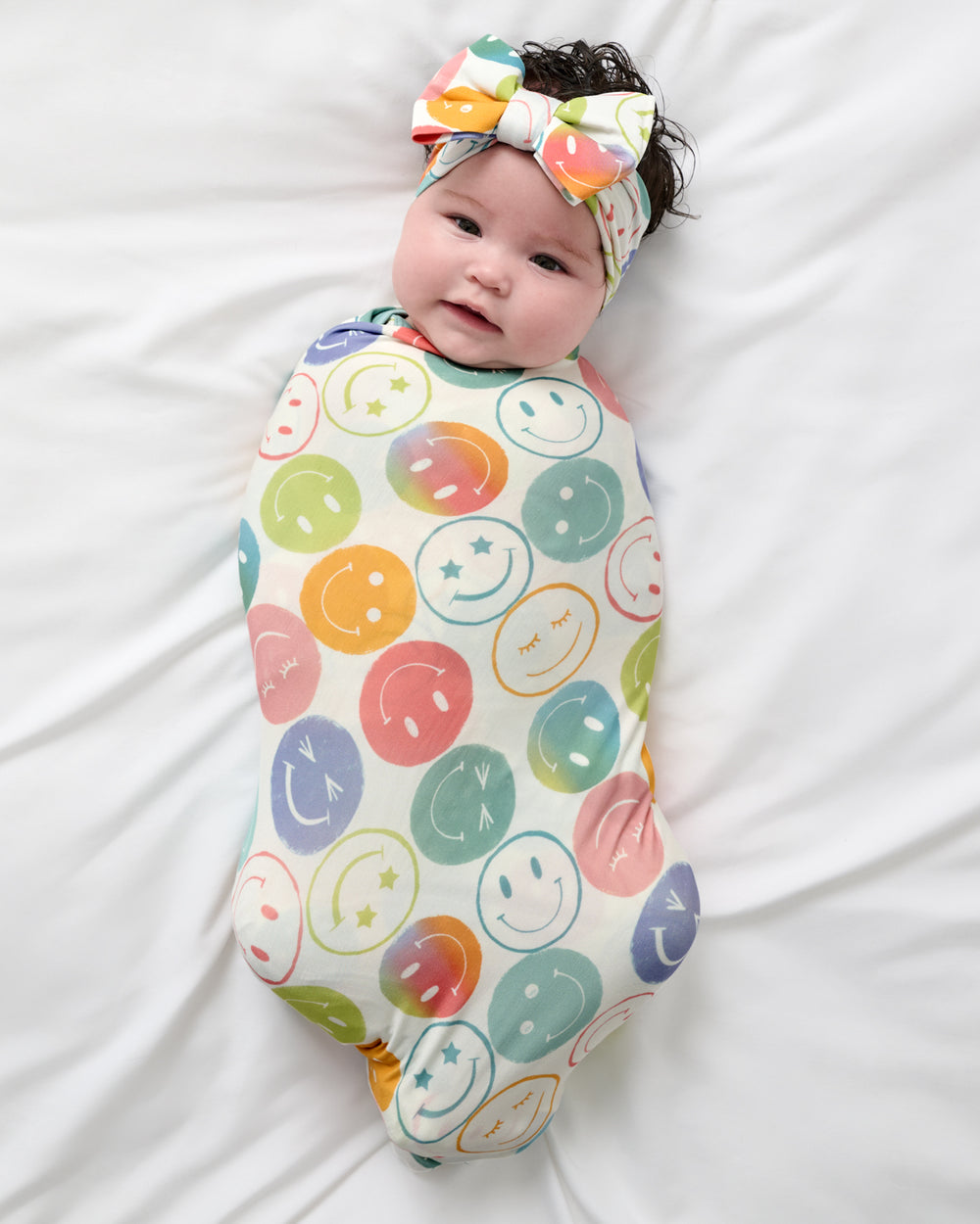 Overhead view of baby wearing the Positive Vibes Swaddle & Luxe Bow Headband Set