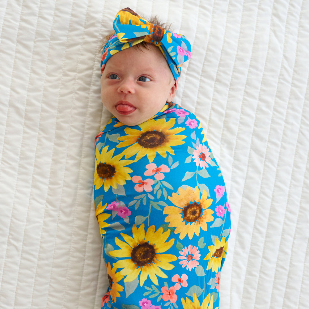 Top view image of baby laying down wearing the Sunflower Fields Swaddle & Luxe Bow Headband 