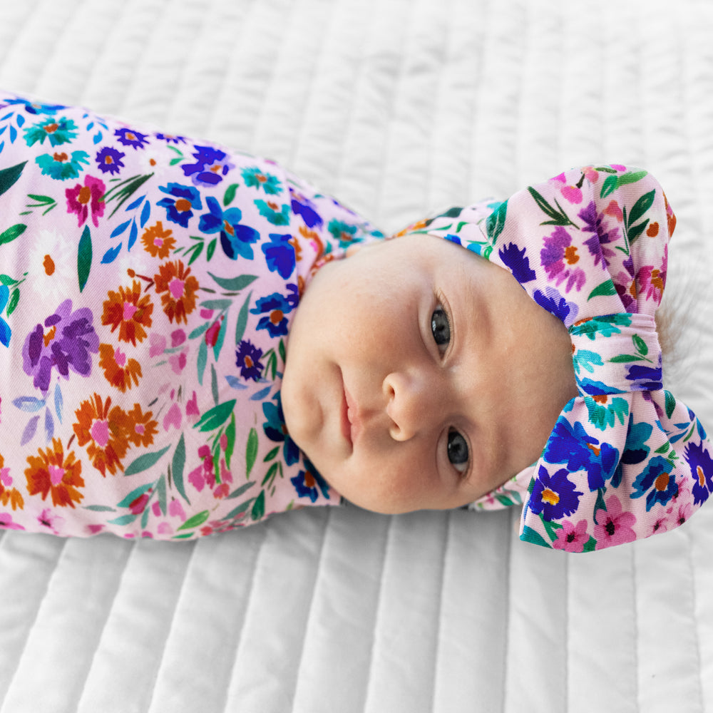 Close up image of a child swaddled on a bed in a Sweet Pea Floral swaddle and luxe bow headband