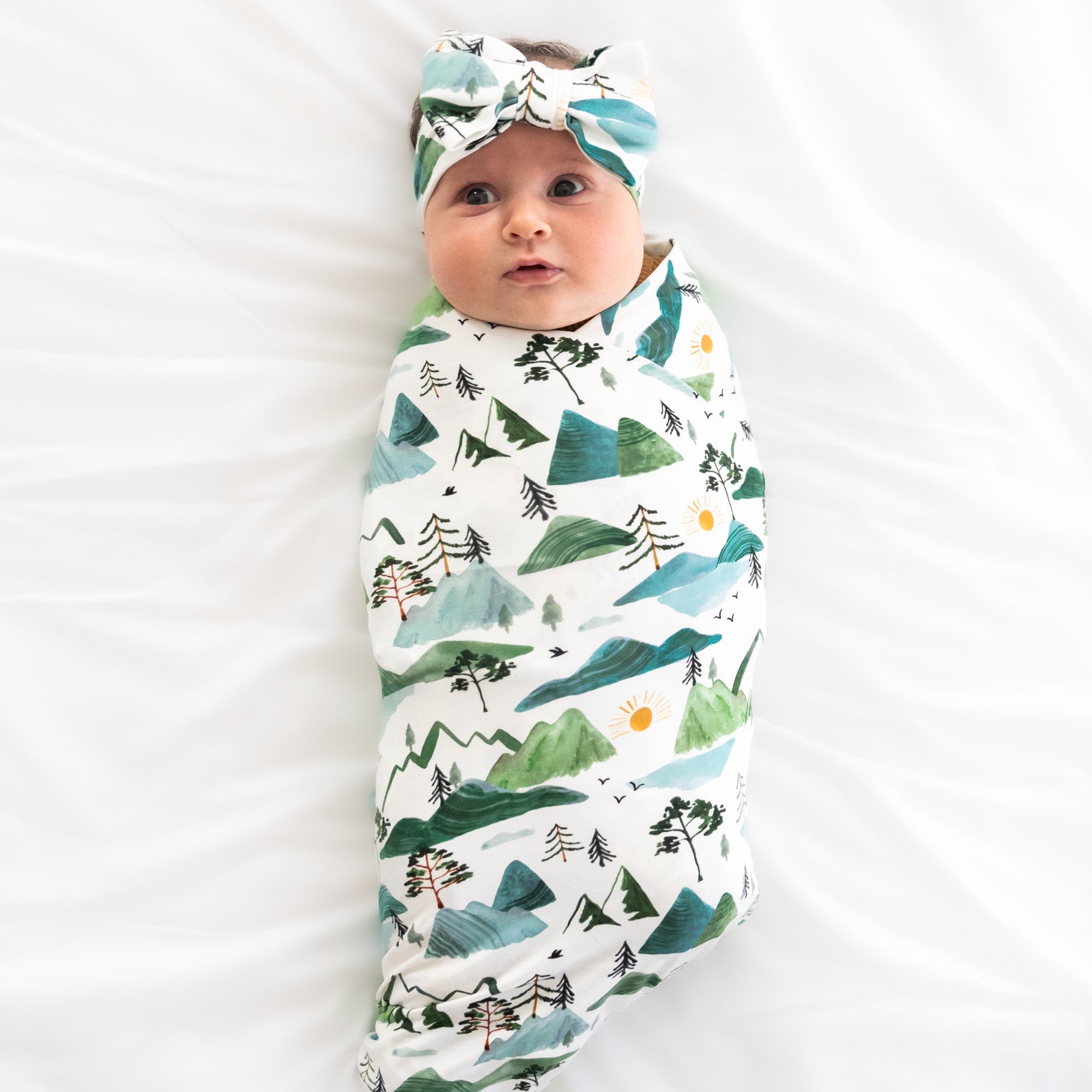 child swaddled on a bed swaddled in a Mountain Mist luxe bow headband set