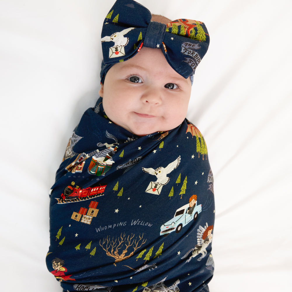 Close up image of a child swaddled in an Evening at Hogwarts swaddle and luxe bow headband set