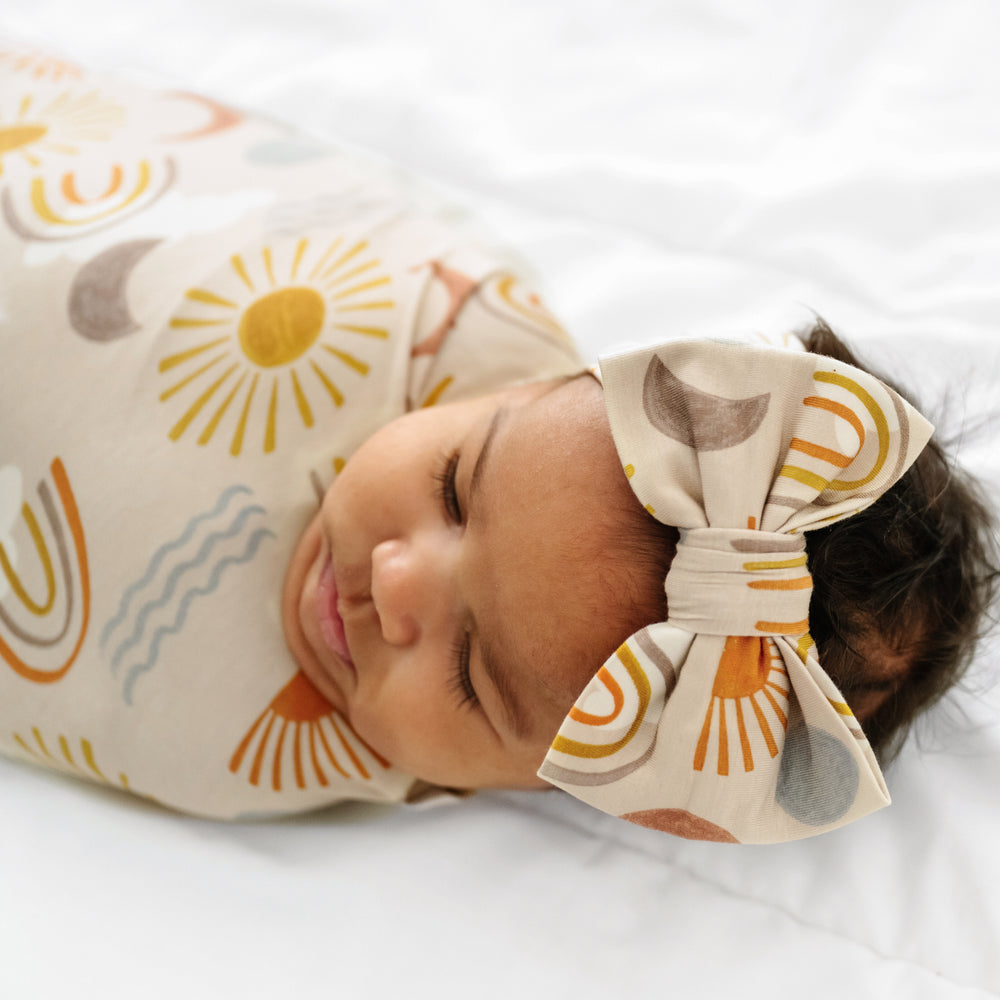 Close up image of a child swaddled in a Desert Sunrise swaddle & luxe bow headband set