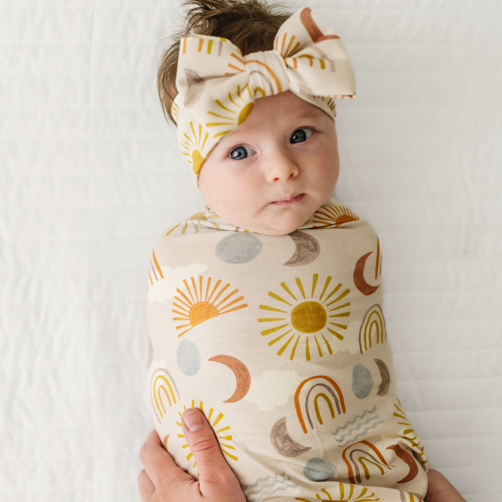 Image of a mother swaddling her child in a Desert Sunrise swaddle and luxe bow headband set
