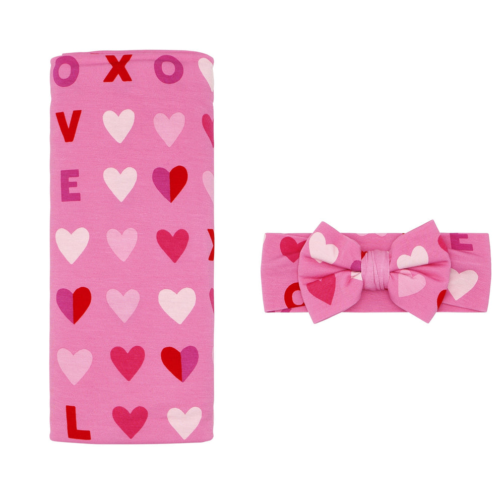 Click to see full screen - Flat lay image of a Pink XOXO swaddle and luxe bow set
