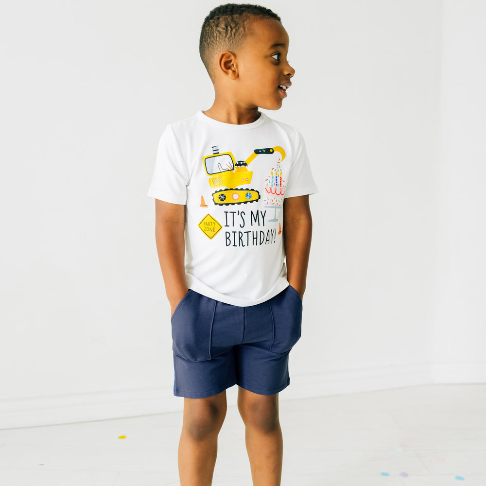 Child posing wearing Birthday Builders construction graphic tee paired with navy shorts
