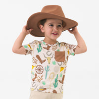 Child wearing a Caramel Ready to Rodeo pocket tee and a cowboy hat
