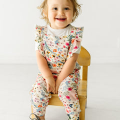 Child sitting on a stool wearing a Mauve Meadow ruffle overall and coordinating Play top