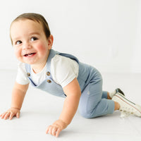 Child crawling on the ground wearing a Fog overall and coordinating Play bodysuit