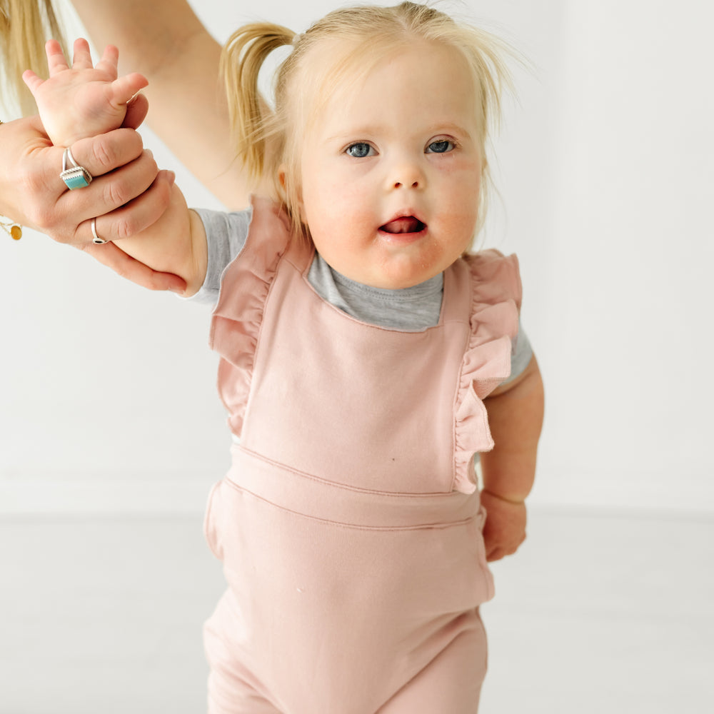 Close up image of a child wearing a Mauve Blush ruffle overall and coordinating Play top