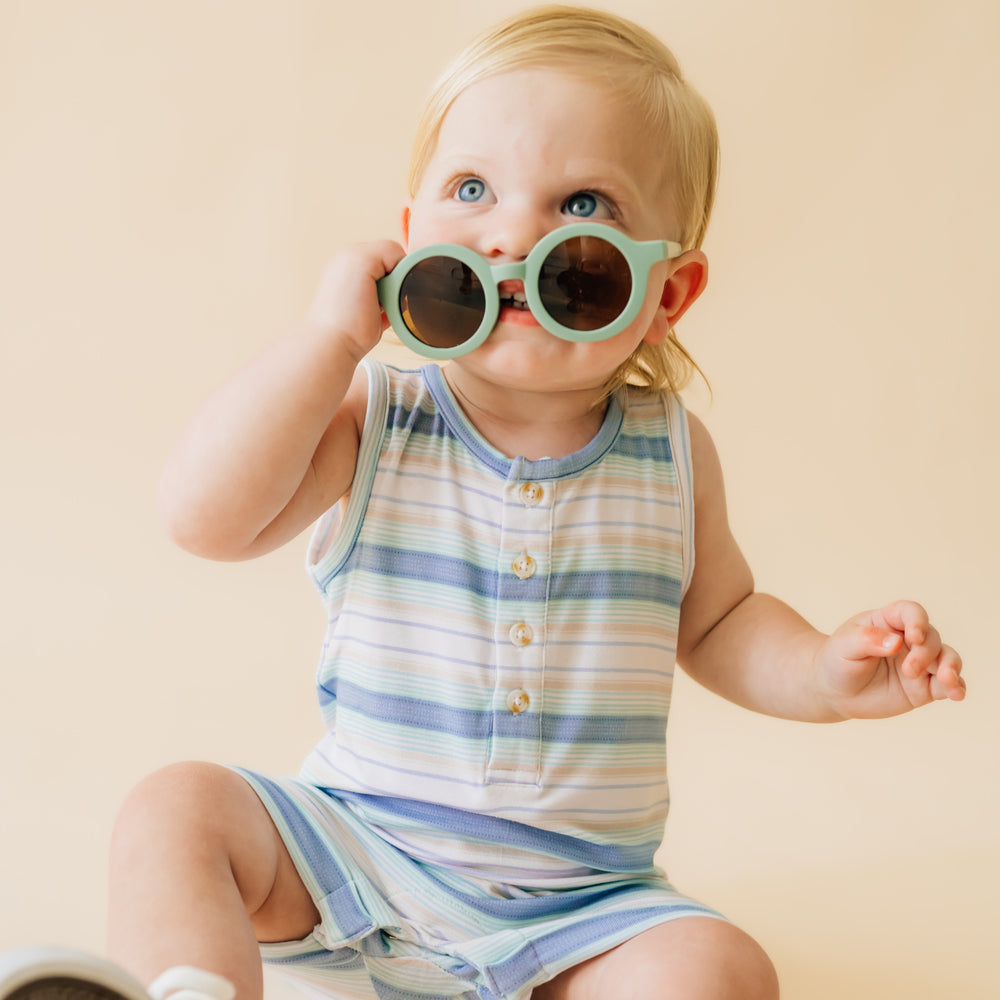 Close up image of a child sitting wearing a Surf Stripe tank button romper