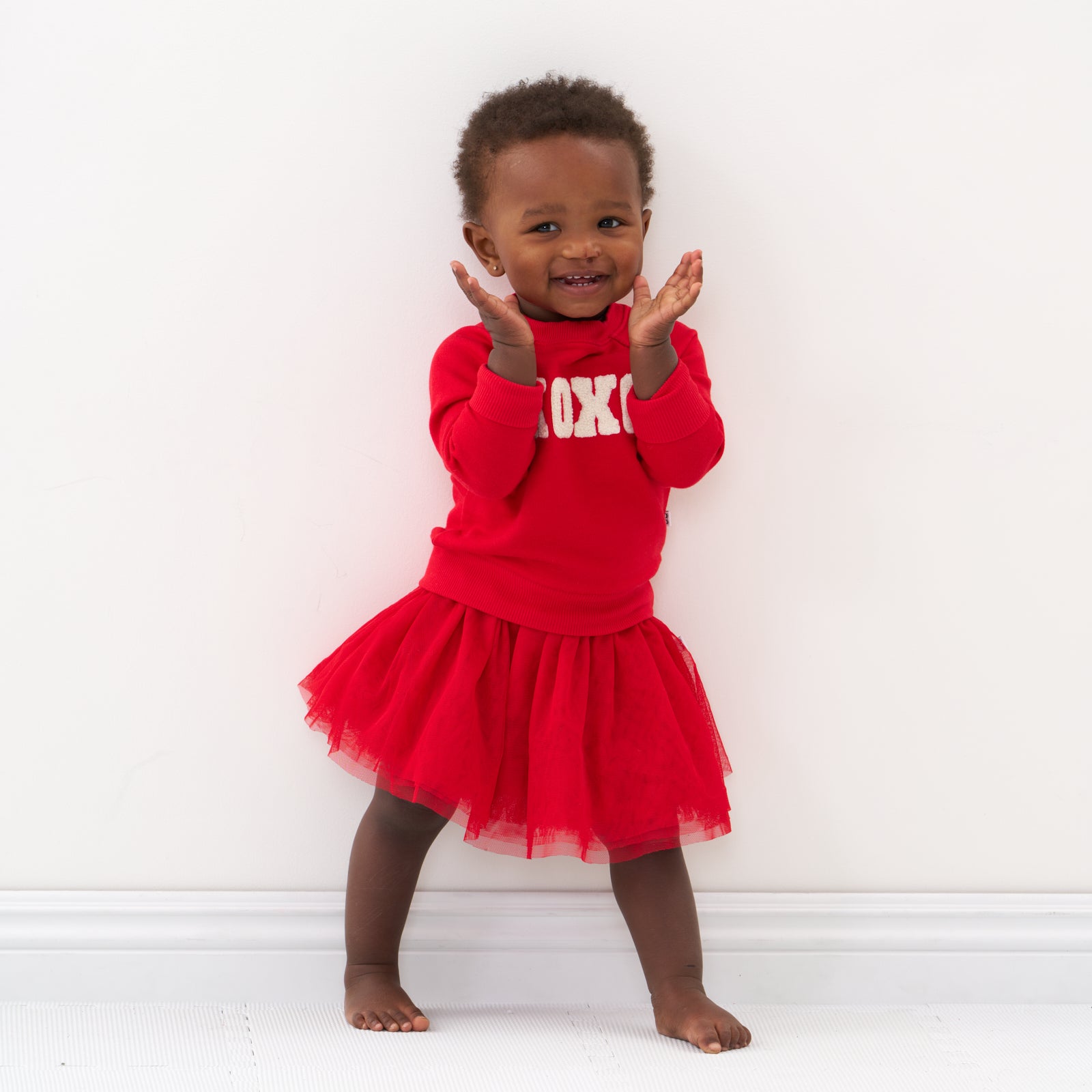 Child clapping her hands wearing a Candy Red tutu skirt and matching crewneck sweater