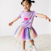 Child twirling wearing a Magical Birthday Light Lavender graphic tee paired with a rainbow tutu skirt