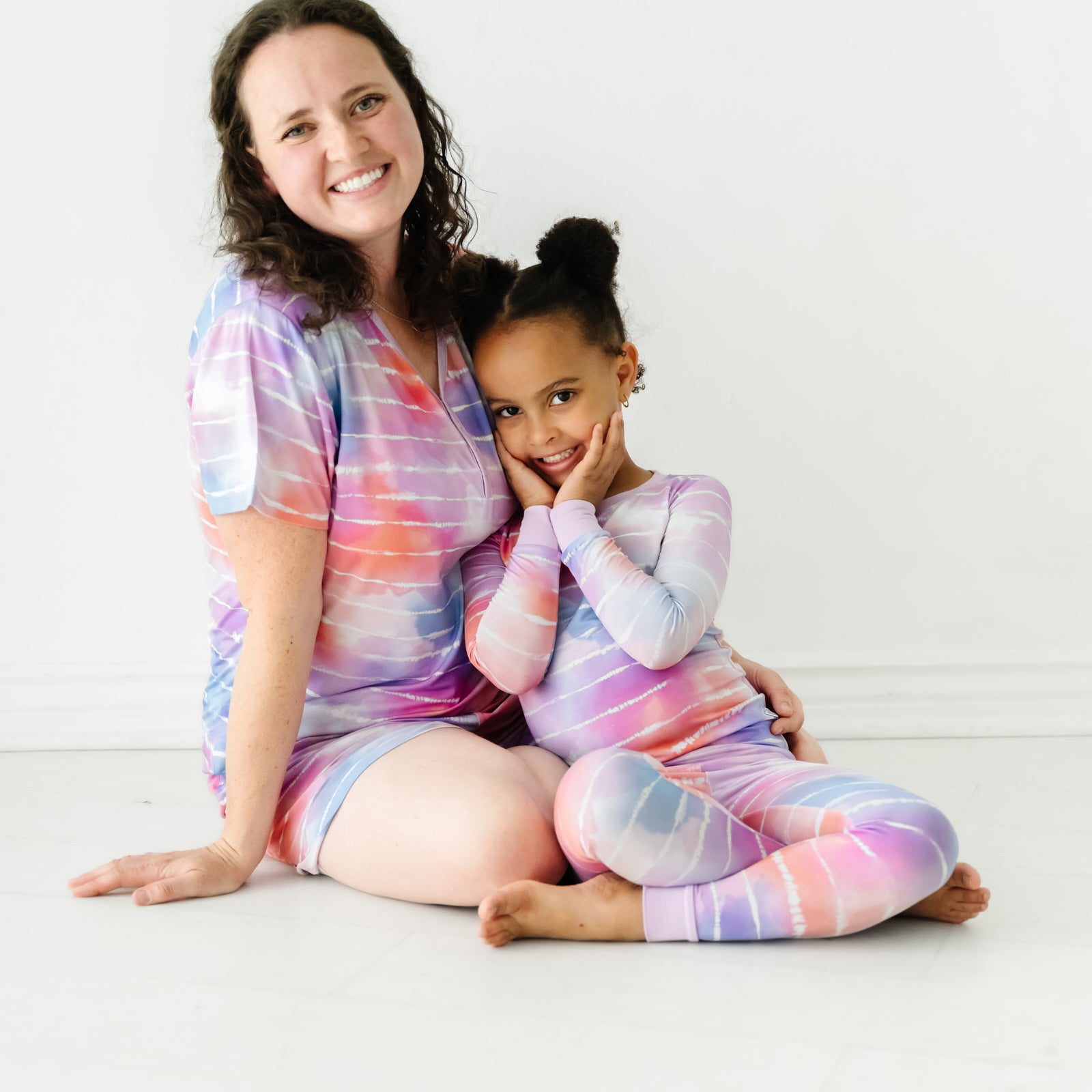 Mother and child sitting on the ground wearing matching Pastel Tie Dye Dreams pajamas